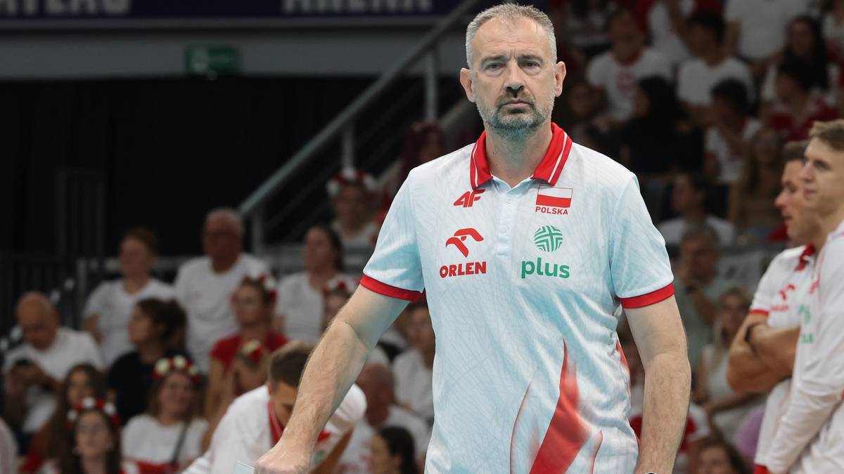 Trener siatkarskiej reprezentacji Polski, Nikola Grbić, w białej koszulce z czerwonymi elementami, stoi na tle publiczności.
