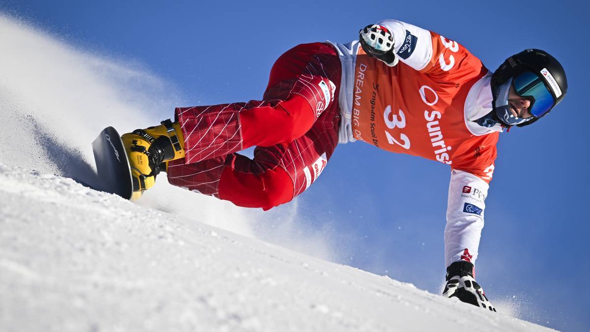 Snowboardzista w czerwonych spodniach i pomarańczowej bluzie z numerem 32 zjeżdża po stoku.