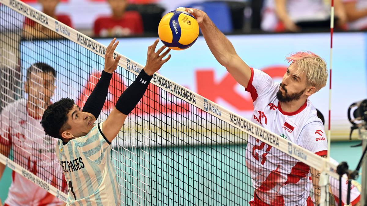 Siatkarz Polski w biało-czerwonej koszulce atakuje piłkę nad siatką, blokowany przez zawodnika Argentyny w jasnej koszulce.