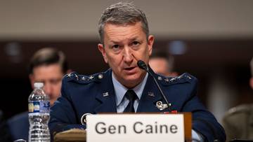Generał Dan Caine przemawia przy mikrofonie, z tabliczką z jego nazwiskiem na stole.