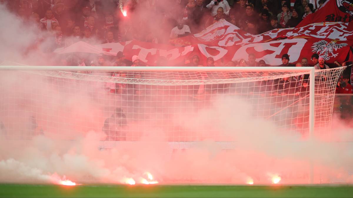 Widok na fragment stadionu z odpalonymi racami i dymem w tle bramki, z kibicami na trybunach.