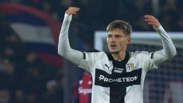 Piłkarz Adrian Benedyczak w białej koszulce z czarnymi wstawkami, z symbolem drużyny Parma, unosi ręce w geście radości po strzelonym golu.