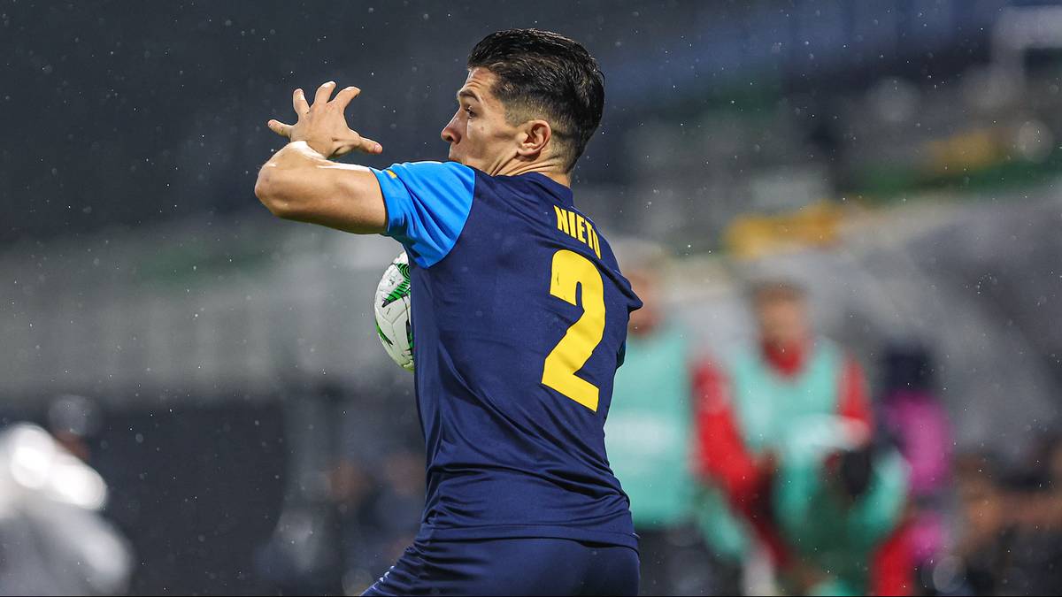 Piłkarz w niebieskiej koszulce z żółtym numerem 2 na plecach łapie piłkę.