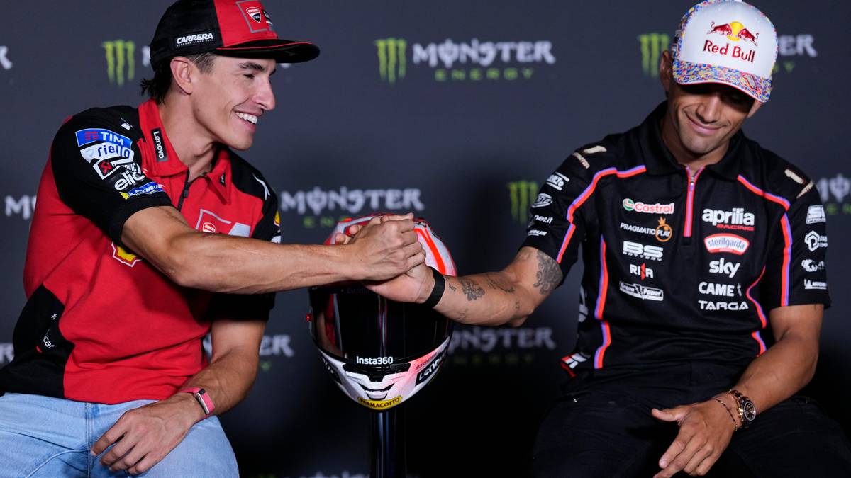 Dwóch motocyklistów ściska sobie dłonie nad kaskiem motocyklowym.