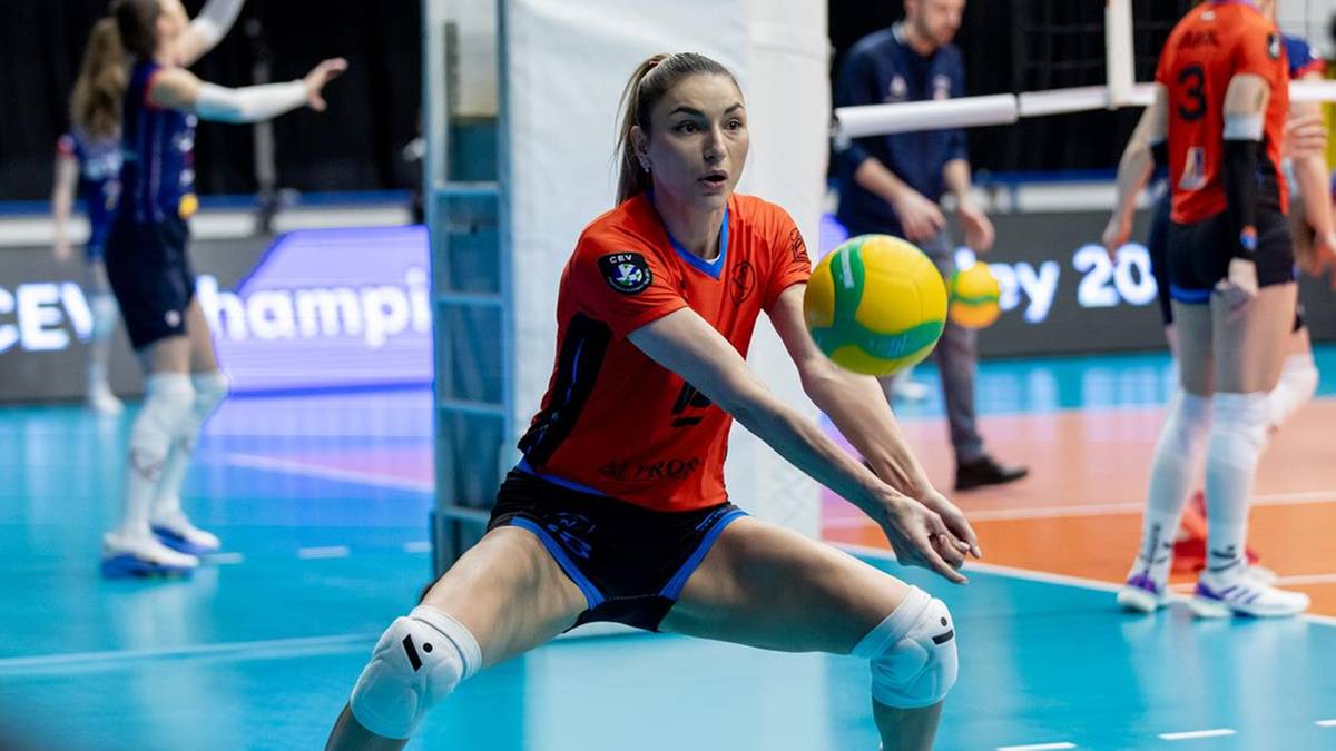 Siatkarka w czerwonej koszulce przyjmuje piłkę w dolnej pozycji na boisku siatkarskim.