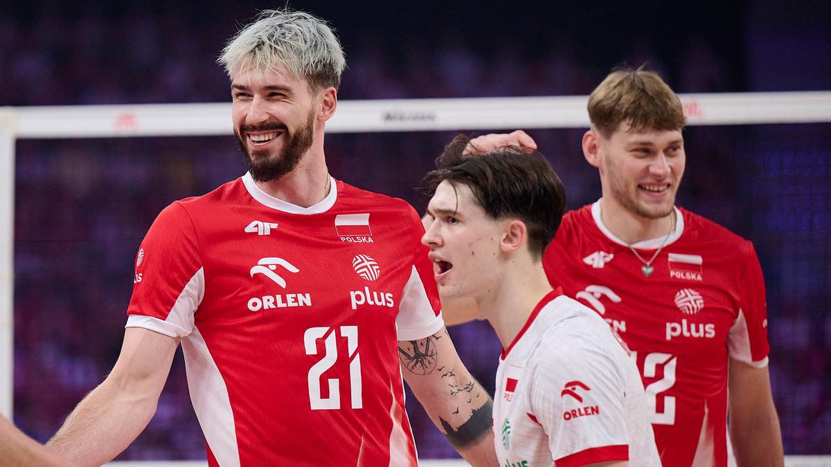 Trzech polskich siatkarzy w czerwonych strojach sportowych z białymi elementami. Dwóch z nich stoi z przodu i uśmiecha się, trzeci stoi z tyłu i patrzy w bok.