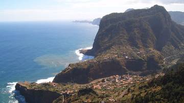 Krajobraz Madery z klifami, oceanem i zabudowaniami na zboczu góry.