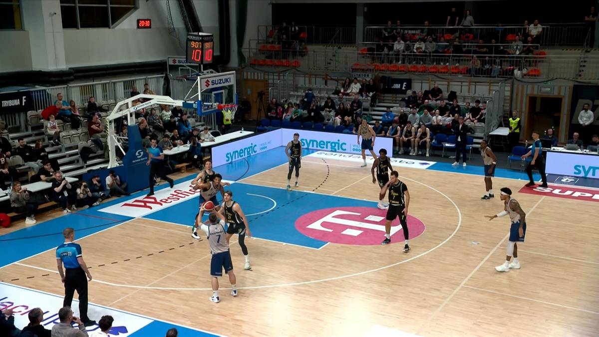 Mecz koszykówki pomiędzy drużynami Dziki Warszawa a BC Dubrava. Zawodnicy w akcji na parkiecie, w tle trybuny wypełnione widzami.