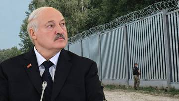 Portret mężczyzny w garniturze, patrzącego w bok, z zamazanym tłem przedstawiającym ogrodzenie z drutem kolczastym.