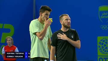 Dw&oacute;ch tenisist&oacute;w na korcie, jeden pr&oacute;buje piłkę, drugi trzyma rękę na piersi.