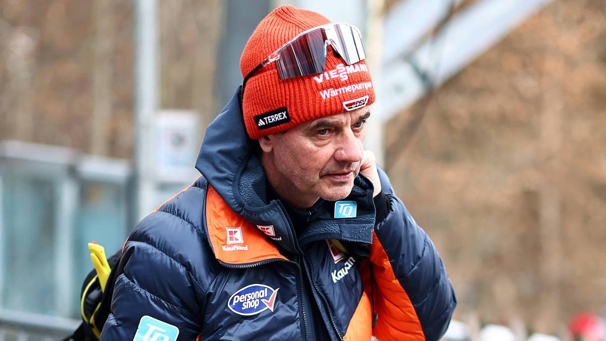 Mężczyzna w pomarańczowo-niebieskiej kurtce puchowej i czerwonej czapce narciarskiej, rozmawiający przez telefon.