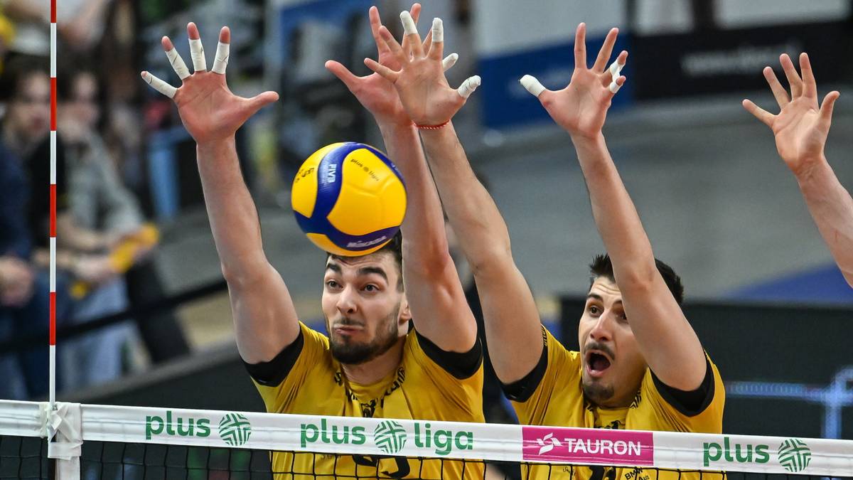 Siatkarze w akcji przy siatce, próbujący zablokować piłkę.