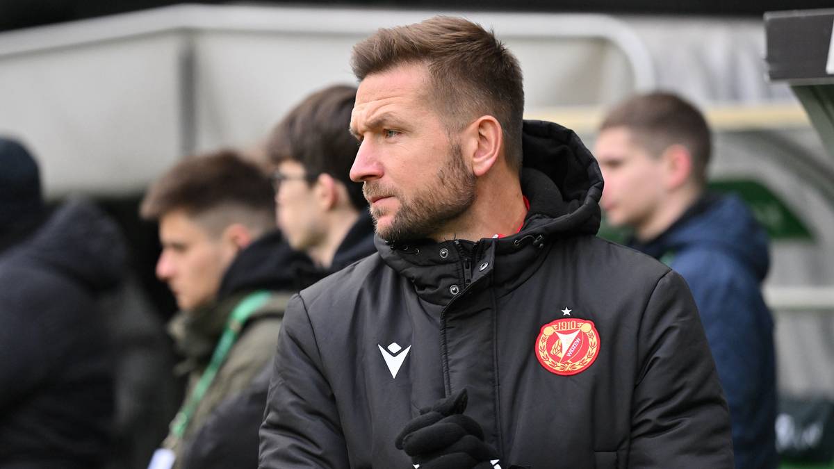 Portret mężczyzny w średnim wieku, ubranego w czarną kurtkę z naszywką klubu sportowego po lewej stronie piersi. Ma krótko przystrzyżone ciemne włosy i kilkudniowy zarost. Patrzy w bok, w jego oczach widać skupienie.