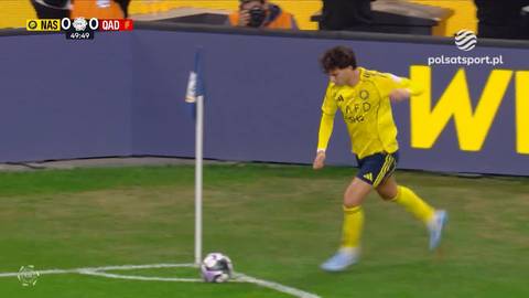 Piłkarz w ż&oacute;łtej koszulce wykonuje rzut rożny na boisku piłkarskim.