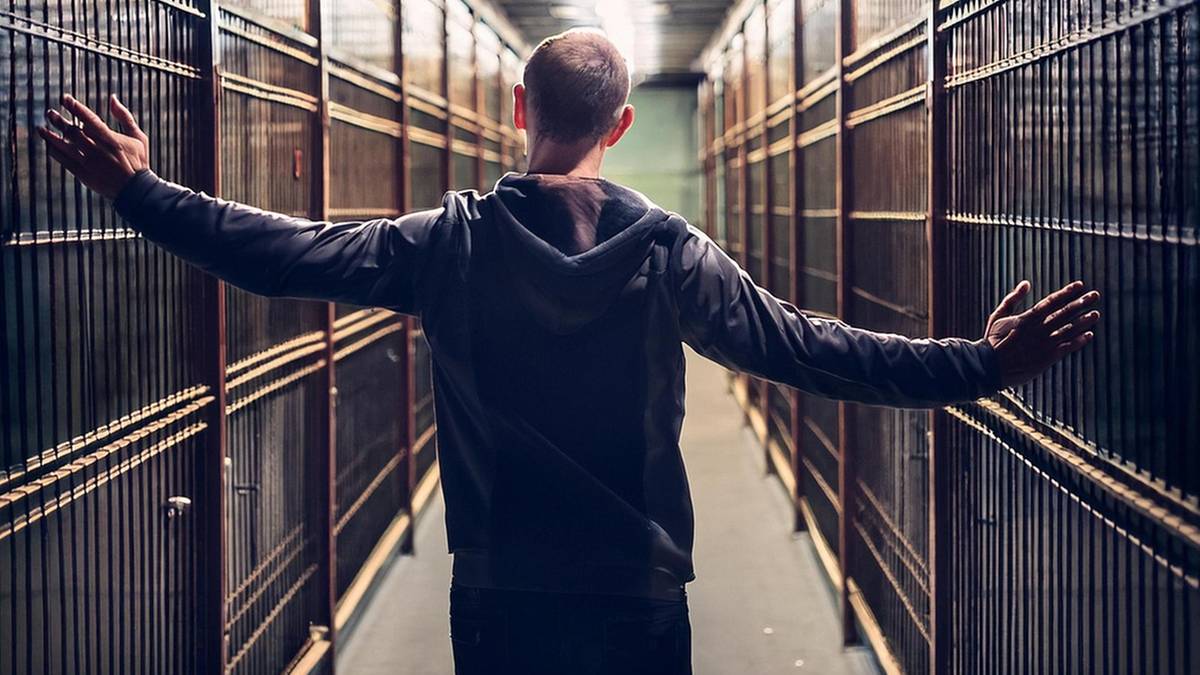 Mężczyzna stoi z rozłożonymi rękami w długim korytarzu z regałami po bokach.