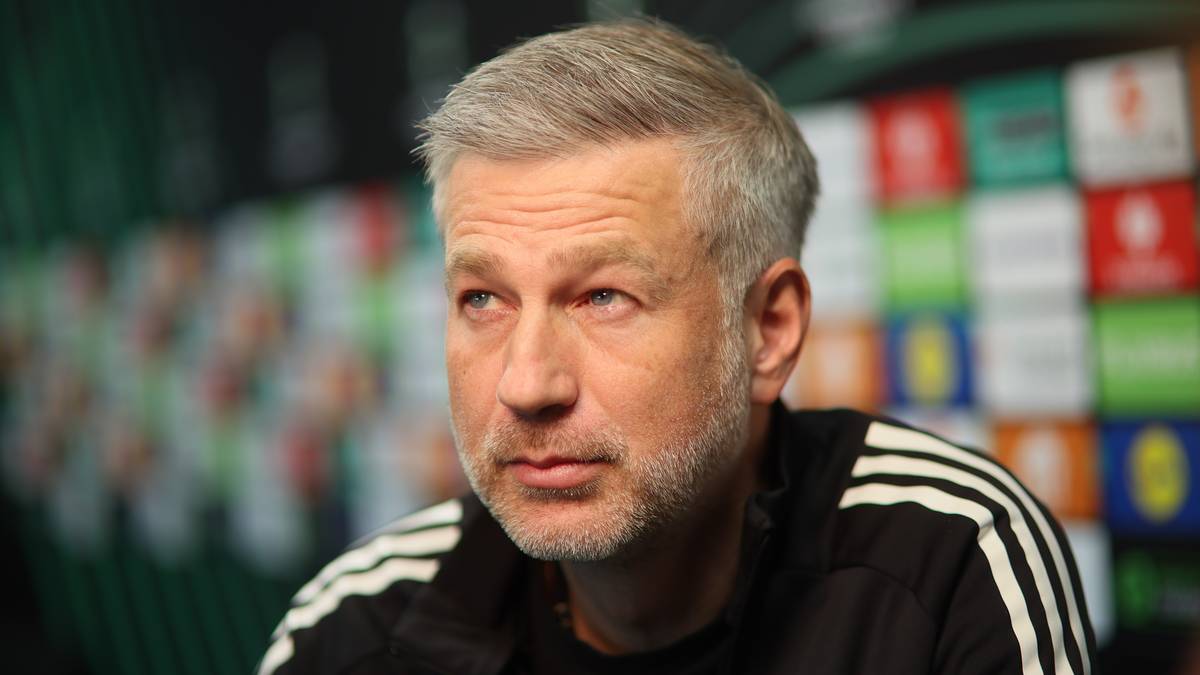 Portret mężczyzny w średnim wieku z siwiejącymi włosami i krótką brodą, ubranego w czarną bluzę z białymi paskami na rękawach.