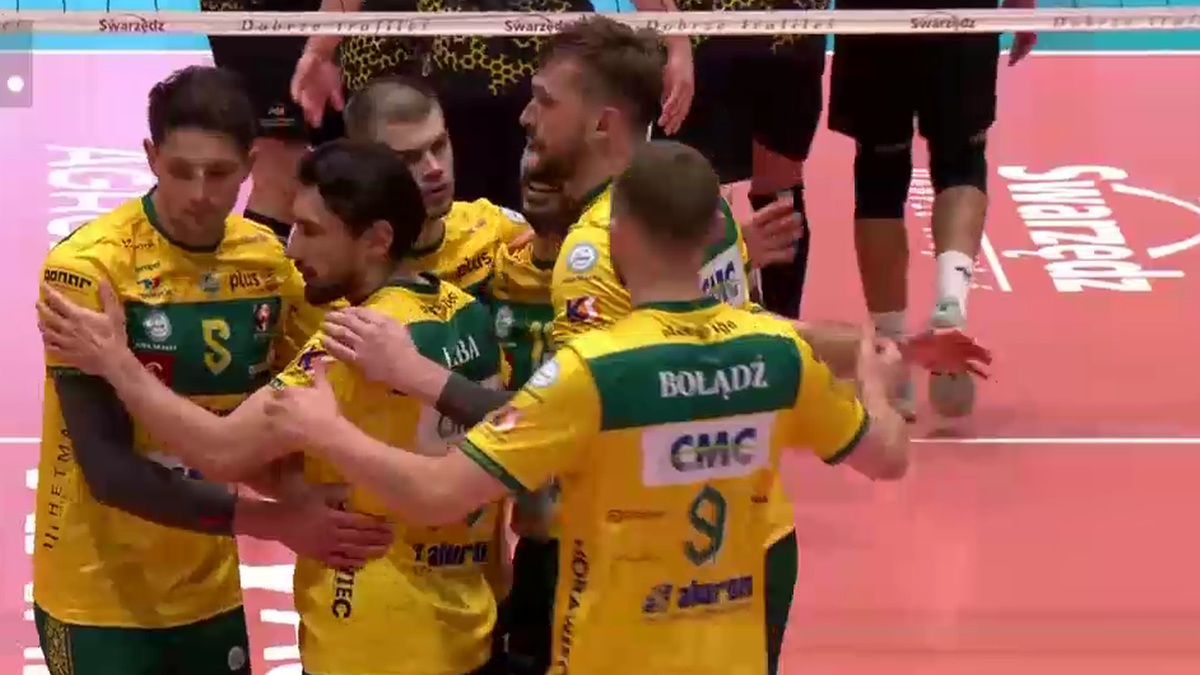 Grupa siatkarzy w żółto-zielonych strojach świętuje zwycięstwo na boisku, przytulając się i unosząc ręce.