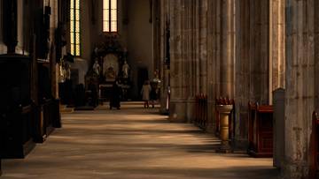 Wnętrze kościoła z rzędem drewnianych ławek po prawej stronie i kolumnami po lewej. W głębi widoczne są okna witrażowe i ołtarz.