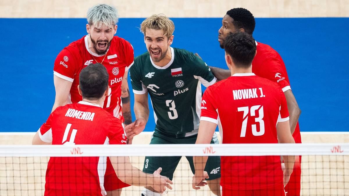 Sześciu zawodników drużyny siatkarskiej w czerwonych i zielonych koszulkach, świętujących zwycięstwo przy siatce. Gracze są podekscytowani, machają rękami i patrzą na siebie.