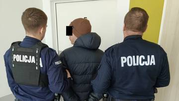 Policjanci prowadzą zatrzymanego mężczyznę w kajdankach.