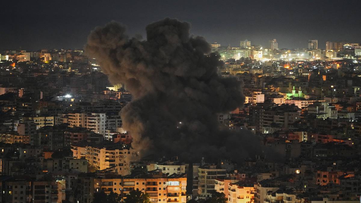 Chmura dymu unosząca się nad zabudowaniami mieszkalnymi w nocy, widoczne światła miasta w tle.