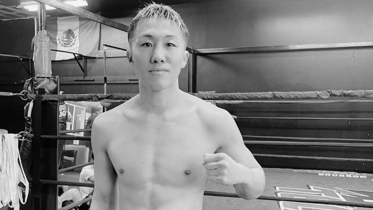 Młody mężczyzna o azjatyckich rysach, w czarno-białym zdjęciu, stoi w ringu bokserskim, patrząc wprost na widza.