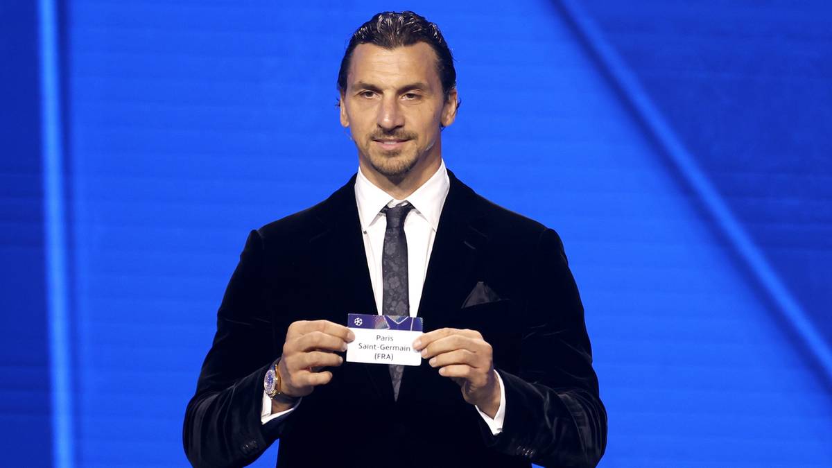 Zlatan Ibrahimović trzyma kartkę z napisem "Grupa A", przed niebieskim tłem.