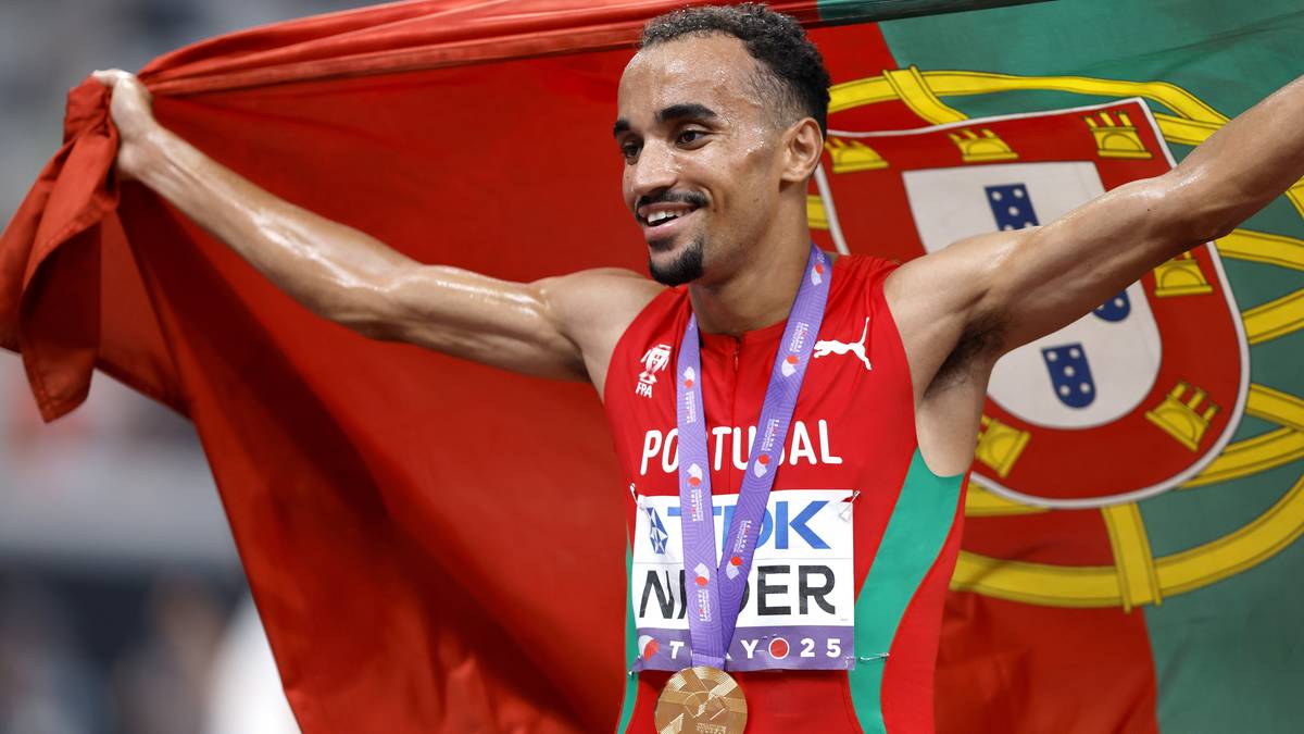 Lekkoatleta z Portugalią z złotym medalem na szyi, trzymający flagę Portugalii, uśmiechnięty.