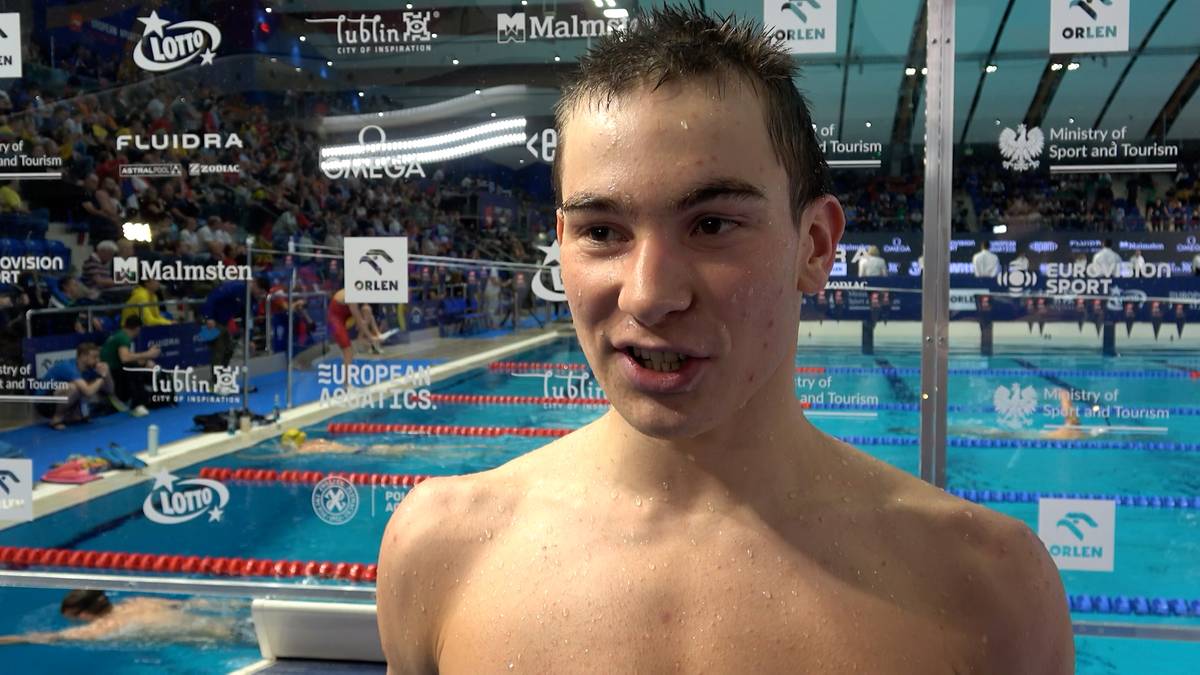 Młody mężczyzna, pływak, podczas wywiadu z basenem i trybunami w tle.