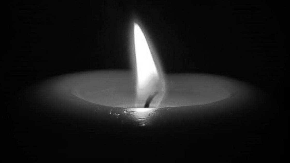 Płonąca świeca na ciemnym tle, symbolizująca pamięć i refleksję.