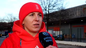 Natalia Czerwonka, polska łyżwiarka szybka, ubrana w czerwoną bluzę z kapturem i czerwoną czapkę, trzyma mikrofon z logo "Polsat Sport" w ręku.