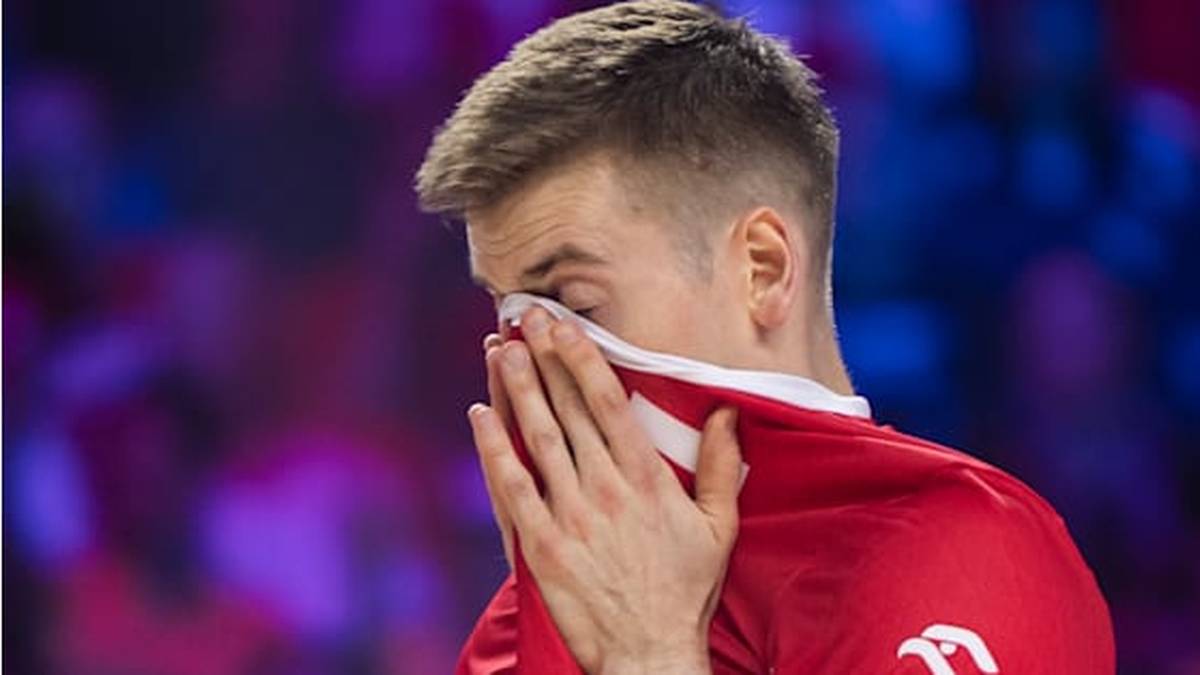 Siatkarz w czerwonej koszulce zasłania twarz ręcznikiem, wykazując oznaki rozczarowania.