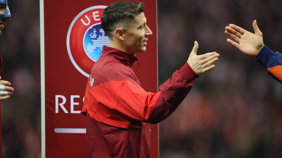 Robert Lewandowski w stroju reprezentacyjnym wychodzi na boisko, witany przez innego zawodnika.