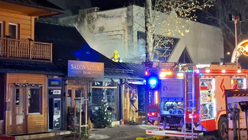 Widok nocą na płonący drewniany budynek restauracji na Krup&oacute;wkach w Zakopanem. Na dachu budynku widoczny strażak w ż&oacute;łtym ubraniu ochronnym. Obok stoi w&oacute;z strażacki z włączonymi sygnałami świetlnymi. W tle widać fragmenty innych budynk&oacute;w i choinkę ozdobioną lampkami.