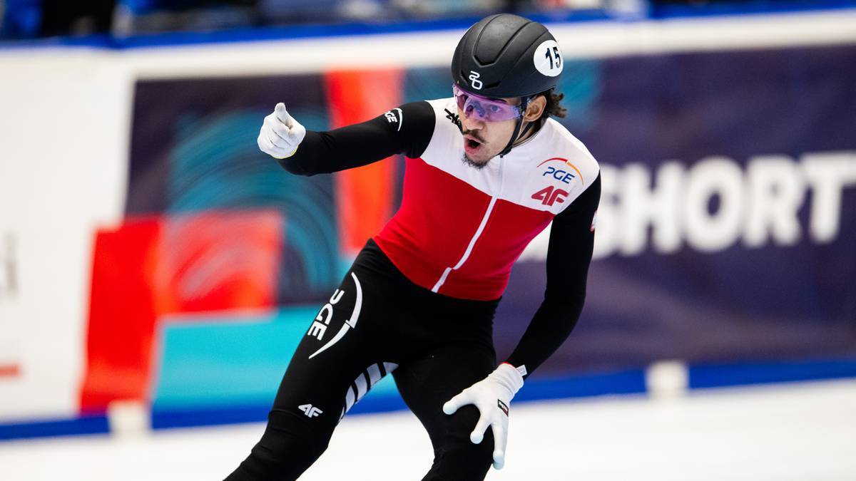 Łyżwiarz szybki w biało-czerwonym kombinezonie pokazuje kciuk w górę.