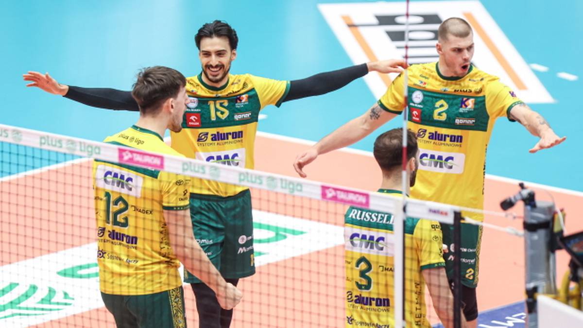 Czterech siatkarzy w ż&oacute;łto-zielonych strojach z numerami na plecach stoi przy siatce, radośnie reagując na wynik meczu.