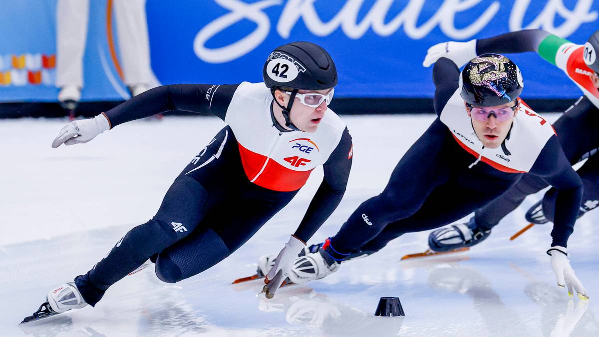 Dw&oacute;ch łyżwiarzy szybkich w strojach sportowych ślizga się po lodzie, jeden z nich ma numer 42 na kasku.