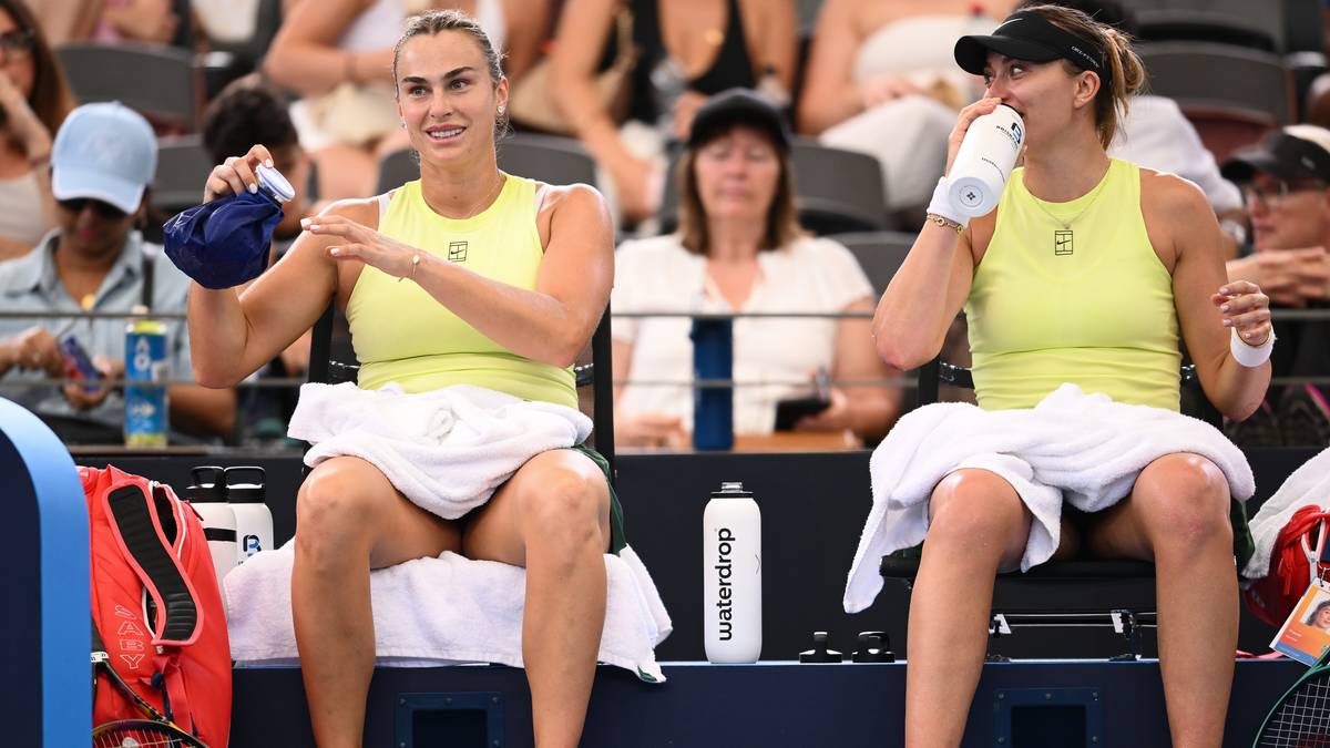 Aryna Sabalenka i Paula Badosa siedzą na ławce podczas meczu deblowego, obie trzymają ręczniki.