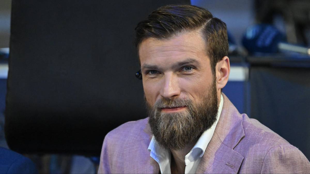 Portret Andrzeja Wrony, ubranego w jasnoróżową marynarkę i białą koszulę, z krótko przystrzyżonymi ciemnymi włosami i zadbaną brodą.