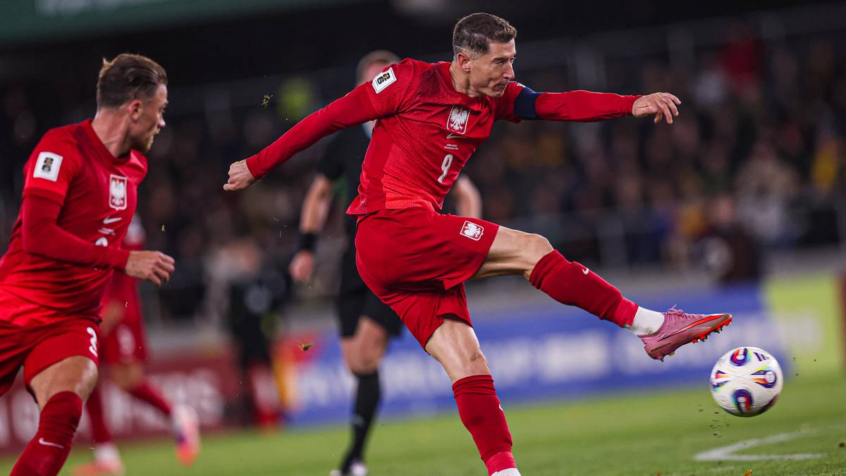 Piłkarz Robert Lewandowski w czerwonym stroju reprezentacji Polski wykonuje strzał do piłki.