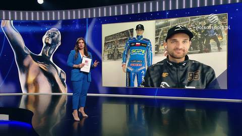 Kobieta w niebieskim garniturze stoi na tle ekranu telewizyjnego. Na ekranie widnieje zdjęcie Bartosza Zmarzlika, a obok niego manekin w kombinezonie żużlowym. Z lewej strony obrazu znajduje się duża, metaliczna rzeźba postaci.