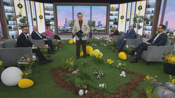 Prezenter stoi na środku scenografii z wiosennymi dekoracjami, otoczony przez siedzących gości.