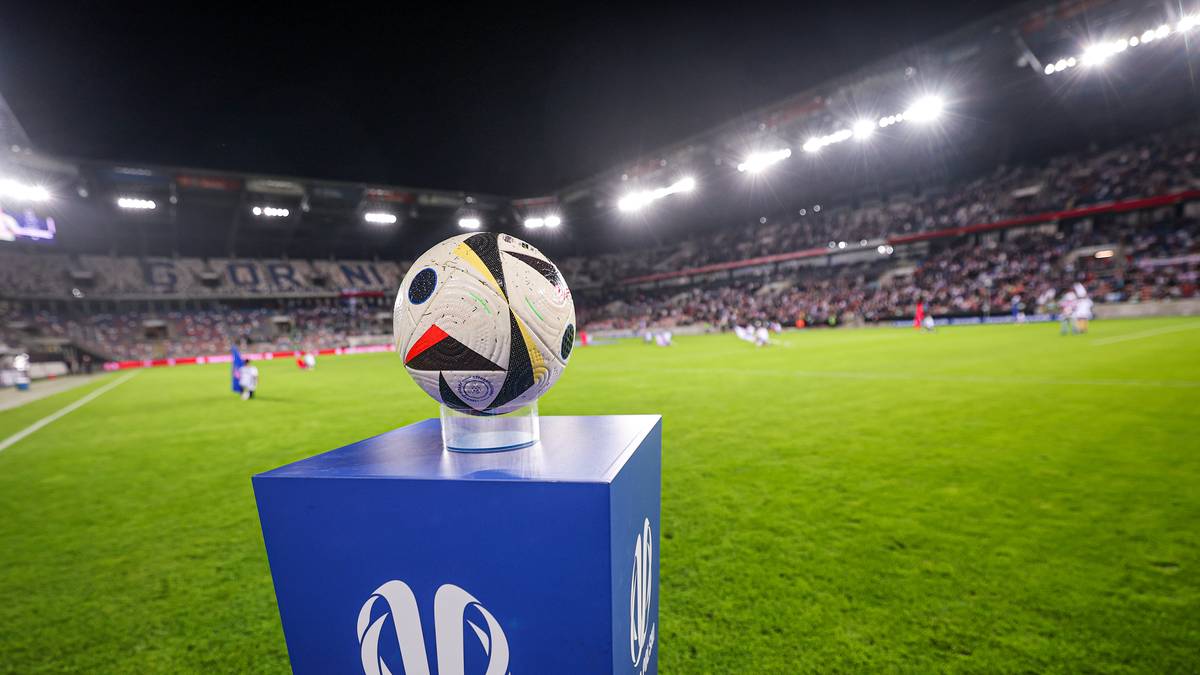 Piłka do piłki nożnej na niebieskim postumencie z logo Pucharu Polski na tle stadionu.