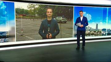 Dwaj mężczyźni w studiu telewizyjnym. Na ekranie za nimi widok placu manewrowego z pachołkami i samochodem.