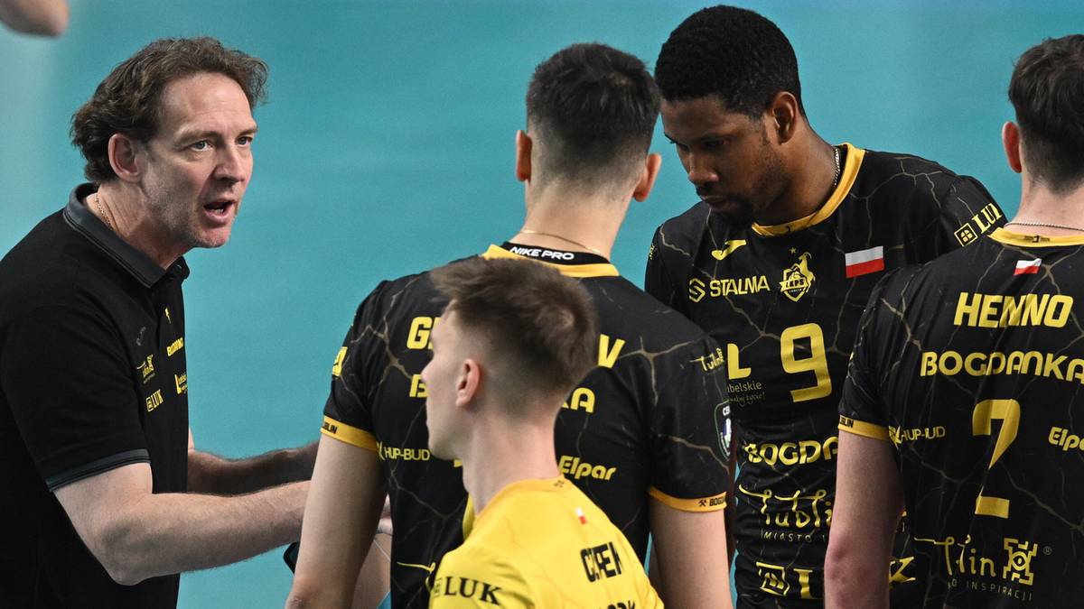 Trener wpatruje się w zawodników w czarnych strojach, gestykulując i udzielając im wskazówek podczas przerwy w meczu siatkówki.