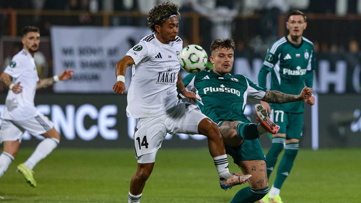 Dwóch piłkarzy walczy o piłkę na boisku.