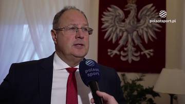 Marian Kmita w garniturze i krawacie z mikrofonem Polsat Sport, w tle godło Polski.