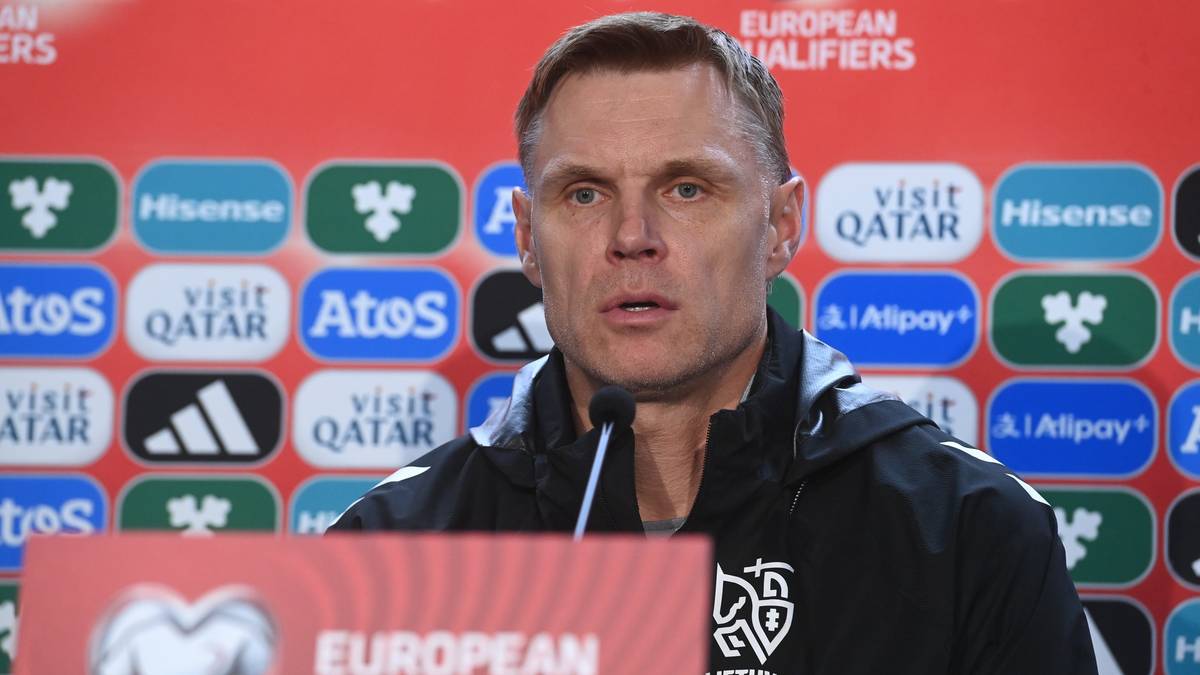 Portret mężczyzny w średnim wieku, mówiącego do mikrofonu na tle ściany z logo "EUROPEAN QUALIFIERS" oraz sponsorów.