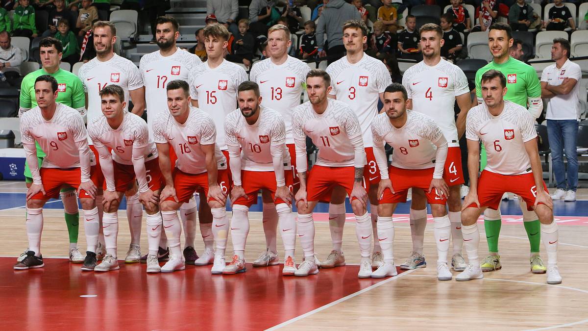 Drużyna piłkarska Polski w białych strojach z orzełkami na piersiach, ustawiona w dwóch rzędach na boisku.