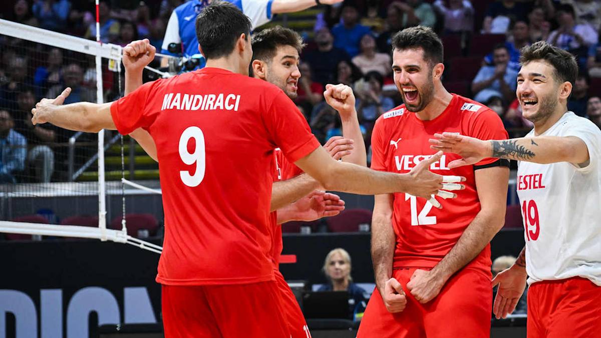 Pięciu siatkarzy reprezentacji Turcji w czerwonych koszulkach, z numerami 9, 12 i 19 na plecach, świętuje zwycięstwo. Dwaj zawodnicy podnoszą ręce do góry w geście radości, jeden uśmiecha się szeroko, a dwaj pozostali przybijają sobie piątki. W tle widać trybuny z kibicami.